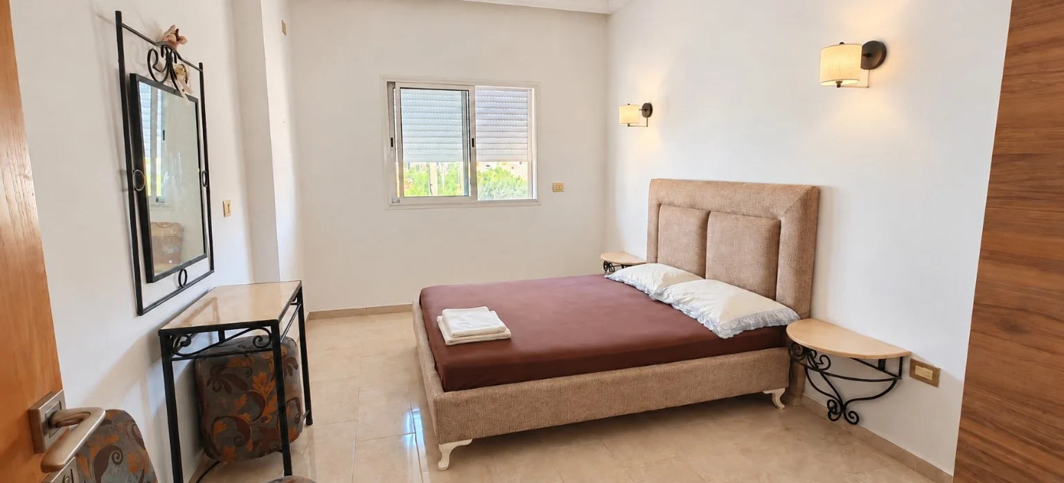 Chambre lumineuse aux tons sable, lit double et appliques murales